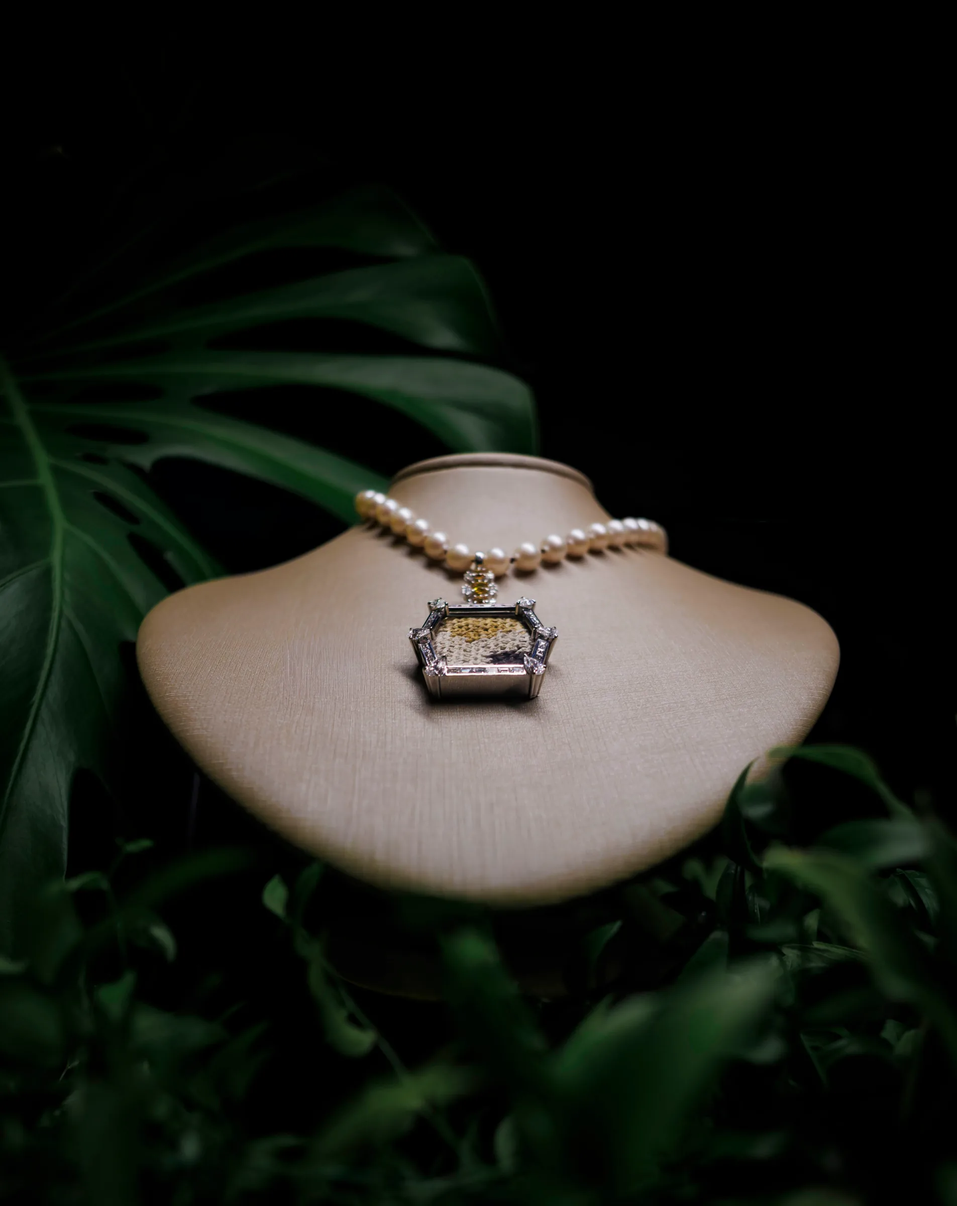 Fibres of Meaning pearl necklace with a woven textile pendant displayed on a bust among foliage